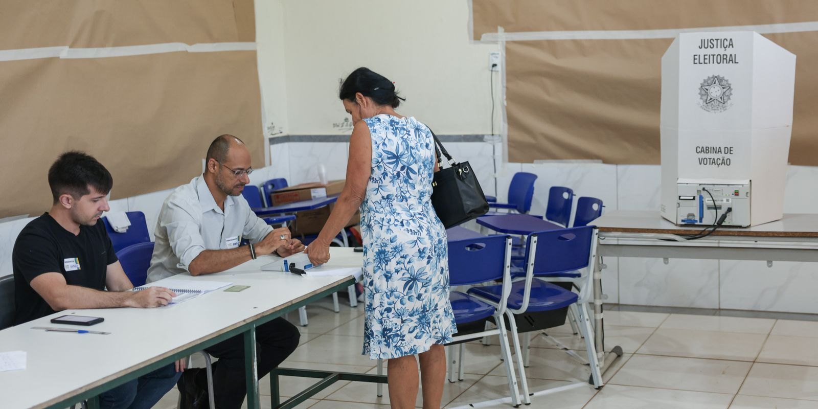 Eleitora se identifica diante de mesários em uma seção de votação