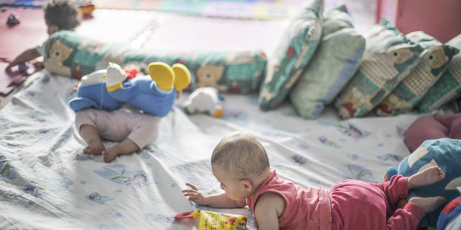 Bebês brincam em um ambiente com colchonetes e almofadas