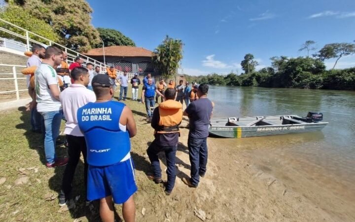 Participantes de atividade da Marinha reunidos à margem de um rio junto a uma embarcação