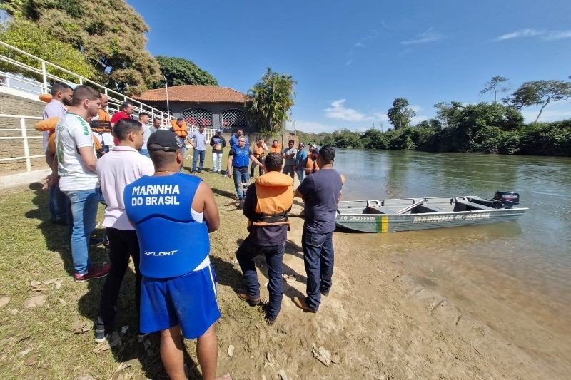 Participantes de atividade da Marinha reunidos à margem de um rio junto a uma embarcação