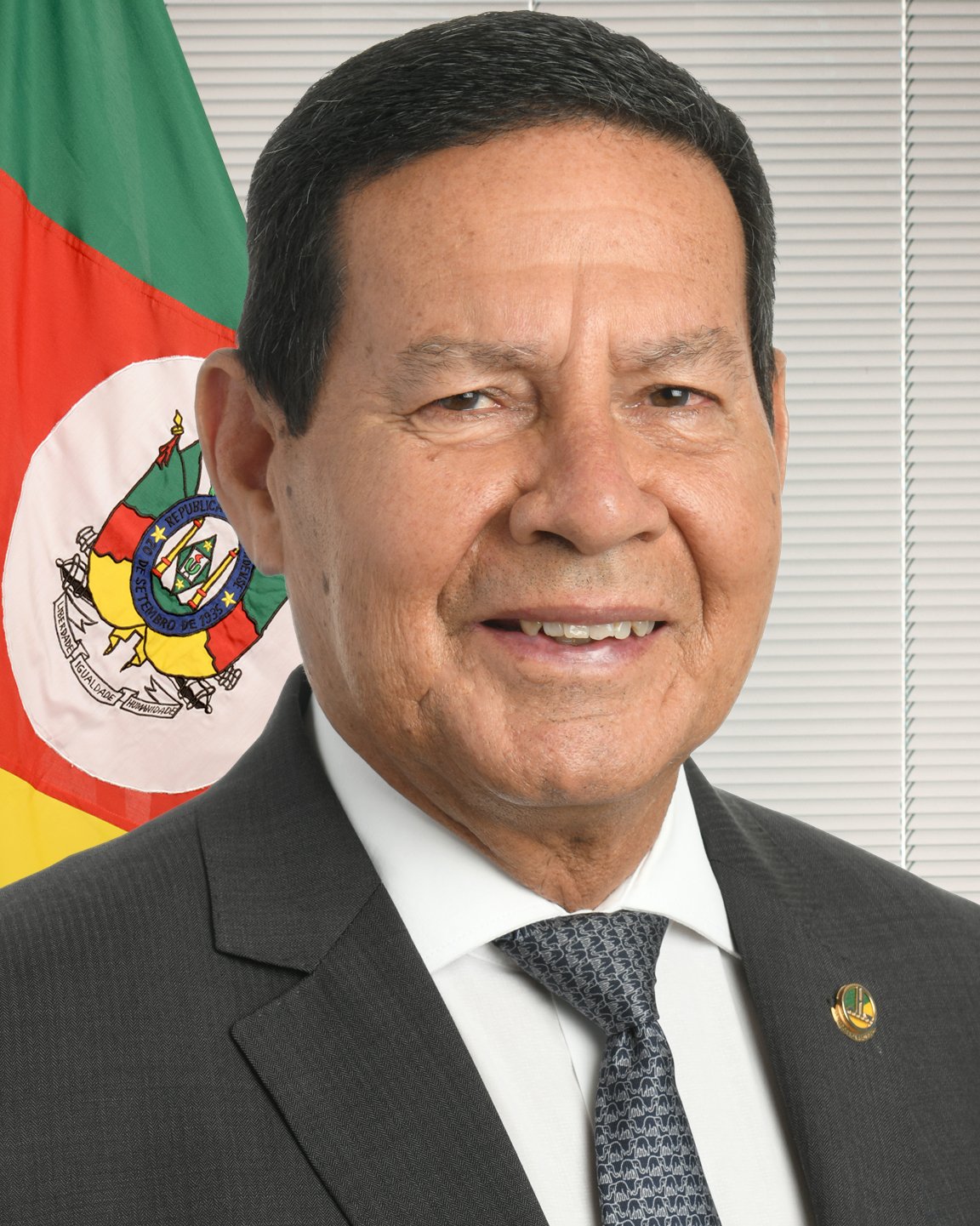 Hamilton Mourão em retrato oficial, de terno e gravata, diante da bandeira do Rio Grande do Sul.