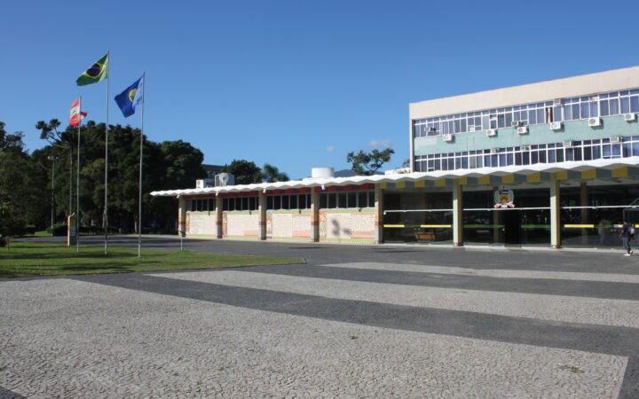 Prédio da Reitoria da UFSC, com bandeiras e a Praça da Cidadania em primeiro plano, em Florianópolis.